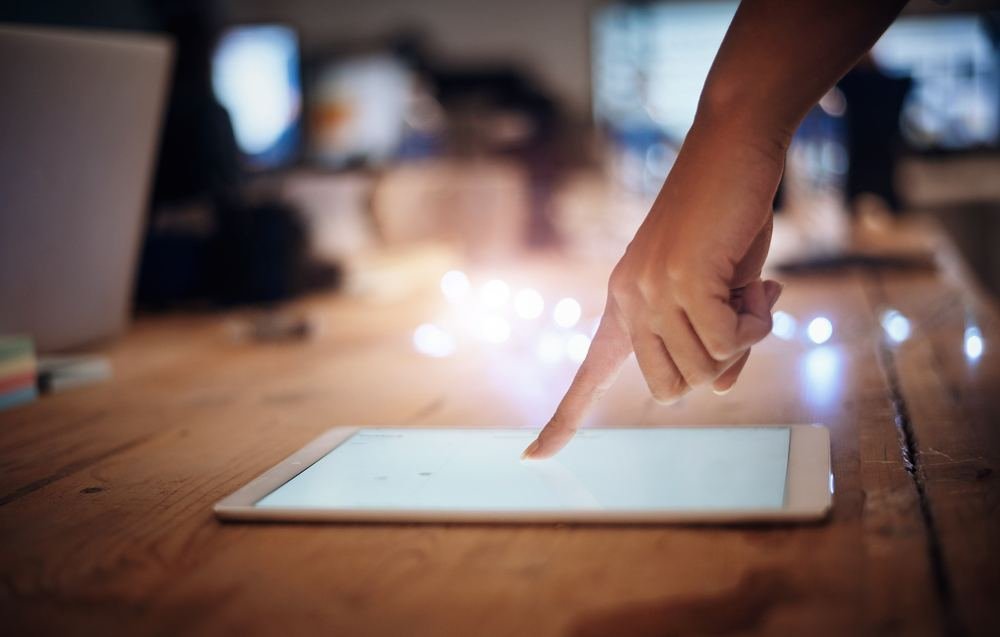 Mano tocando la pantalla de una tableta sobre una mesa de madera